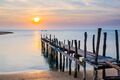 Alter Pier oder eine Holzbrücke wird bei Sonnenuntergang am Strand ins Meer gebr