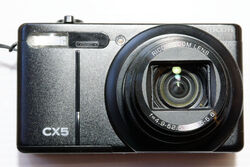 Ricoh CX5, 10x Zoom, handliche kleine Digitalkamera in schwarz, Aufnahmebereit.